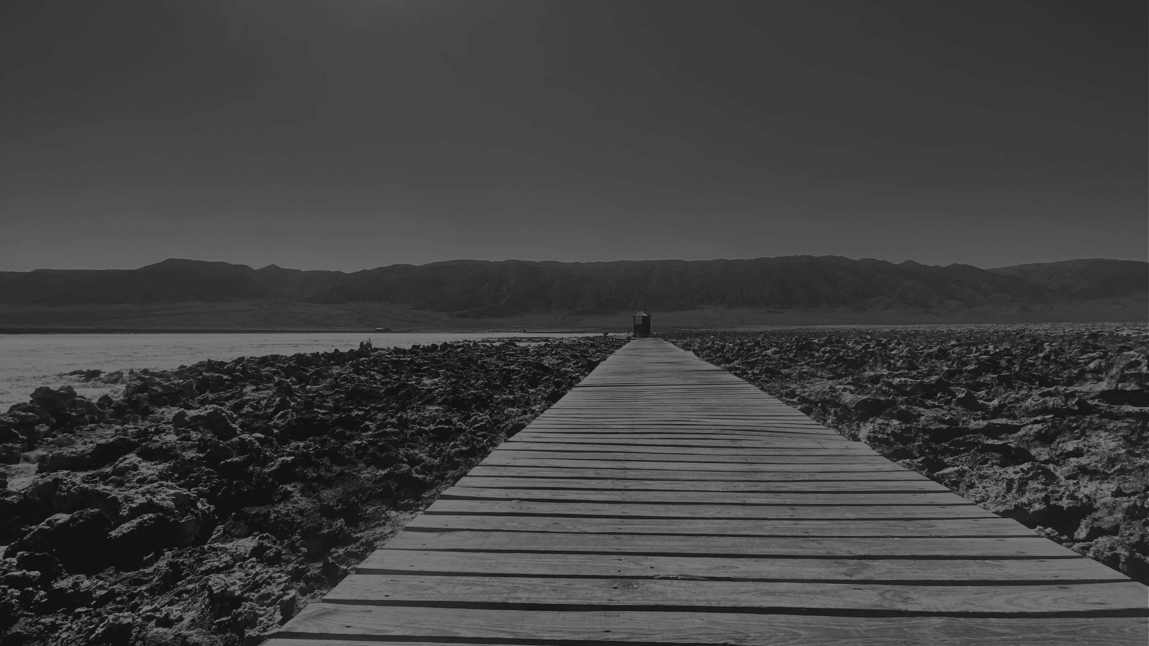 A wooden boardwalk stretching toward distant mountains across a vast salt flat